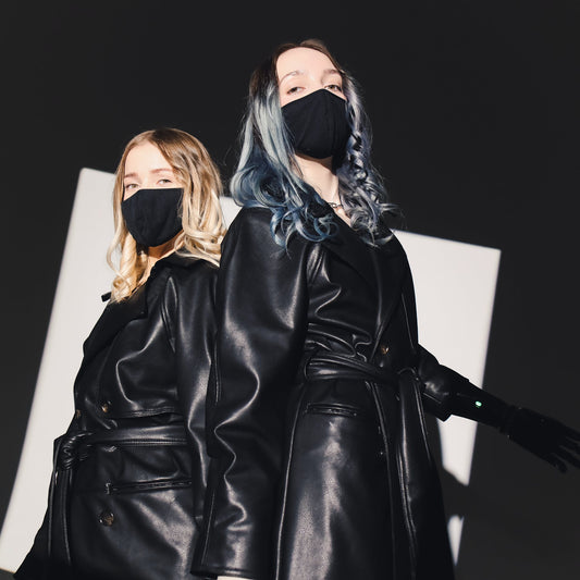 photo of women standing back to back wearing black coats and black masks with hair open